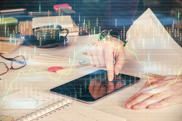 Double exposure of man's hands holding and using a digital device and forex graph drawing. Financial market concept.