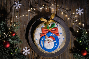 Ornate gingerbread decorated with Santa smiling from Xmas bauble. Christmas flat lay with fir twigs, red baubles and paper snowflakes. Dark wooden planks, top view of rustic wooden table.