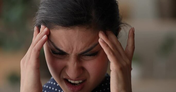 Close up frustrated unhappy stressed young indian ethnicity woman irritated by loud noise in neighborhood, suffering from sudden headache migraine or high blood pressure, feeling unhealthy unwell.