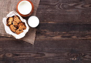 Chocolate cookies and milk in glass and pot on burlap on a wooden table.