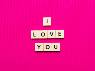 I LOVE YOU text made from square letter tiles on pink background.