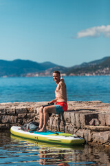 A young athletic man enjoys SUP Stand up paddle boarding on a sunny day in Montenegro. Island Gospa od Milosti in Montenegro.