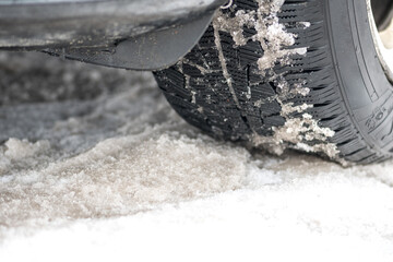 Close up winter tire of a car on the road covered by snow and ice driving in extreme cold temperature