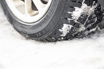 Close up winter tire of a car on the road covered by snow and ice driving in extreme cold temperature