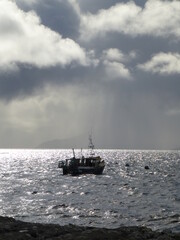 Naklejka premium Fishing boat seen against a stormy sea and sky off Elgol, Isle of Skye