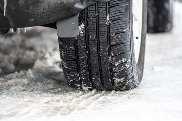 Close up winter tire of a car on the road covered by snow and ice driving in extreme cold...