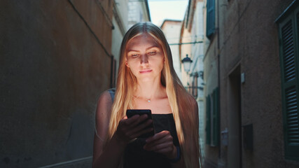 Close-up of blonde woman sharing her impressions from summer trip on video call on smartphone while walking the city of her visit
