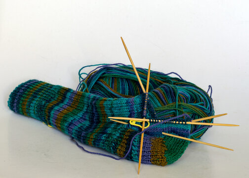 Knitted Sock Knitted With Green Striped Yarn, Wooden Knitting Needles And A Ball Of Wool Yarn, Handicrafts As A Hobby, Knitting Concept