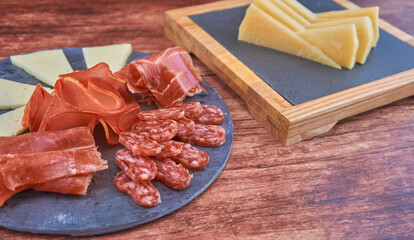 BODEGÓN DE RACIÓN DE QUESO MANCHEGO Y JAMÓN Y LOMO SOBRE FONDO DE MADERA