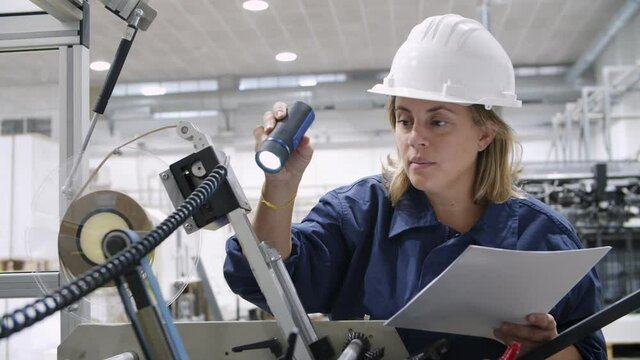 Serious female factory worker checking equipment specifications and holding flashlight. Pensive blonde technician working on paper plant. Slider motion. Visual inspection and manufacture concept