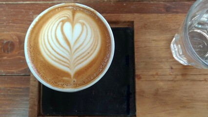 Heart shaped latte art is on the wooden table.