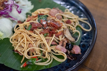 Spicy spaghetti with bacon and basil served on banana leaf.