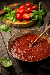 Classic homemade Italian tomato sauce with basil for pasta and pizza in the pan on wooden background.