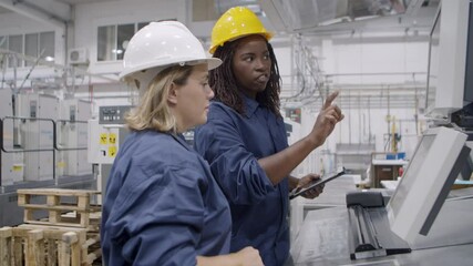 African American female factory engineer teaching employee to use new machine, explaining operating process. Industry or machinery concept
