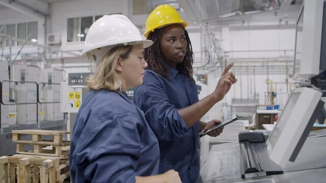 African American female factory engineer teaching employee to use new machine, explaining operating process. Industry or machinery concept