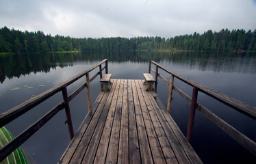 A wooden bridge on a lake in the forest, green fir trees and a cloudy sky. Tourist holidays on the Karelian Isthmus.