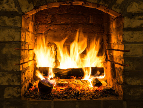 Burning firewood in fire-box of fireplace in country cottage.  Orange light of flame and embers warmth.