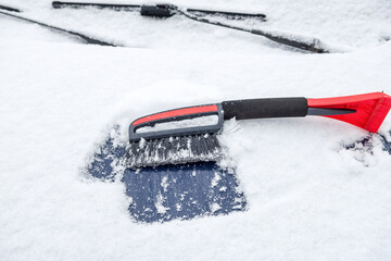 Snow cleaning brush lies on the car windshield in the open air.