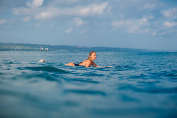 Attractive surfing woman with surfboard. Surfgirl paddle on surfboard in ocean