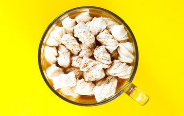 Cocoa drink with marshmallows in glass mug on yellow background top view