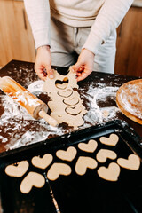 Cookies in shape of heart for the Saint Valentine's Day. Man is baking heart shape cookies for Saint Valentine's Day. Dough, flour, baking pan, round wooden cutting board and rolling pin on the table.