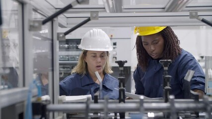 Diverse female factory engineers using paper manual and tablet, studying and testing new industrial machine . Production process or machinery concept - Powered by Adobe