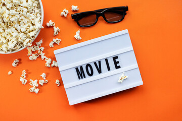 Popcorn, 3D glasses and lightbox text Movie time on orange paper background. Top view Template