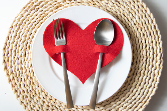 St Valentine's table setting with festive decorations on a wicker stand, with white plate, a fork with a tablespoon with red heart on it