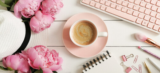 White wooden home office table with summer hat, pink peony flowers, cup of coffee, computer and notebook. Top view. © sunfe