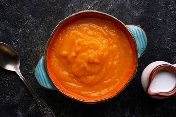 baked pumpkin cream coup with  coconut milk served in nice bowl at wooden black table. flat lay. cooking and healthy life concept