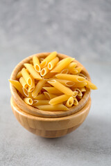 Uncooked yellow pasta in a wooden bowl on gray table. Selective focus. Italian food concept. Vertical orientation