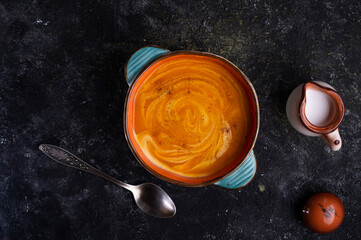 baked pumpkin cream coup with  coconut milk served in nice bowl at wooden black table. flat lay. cooking and healthy life concept