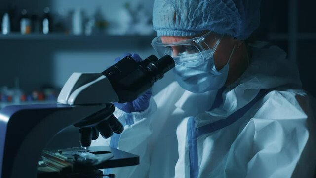 Woman scientist is looking into microscope. Biochemical research scientist is working with microscope for coronavirus vaccine development in pharmaceutical research laboratory