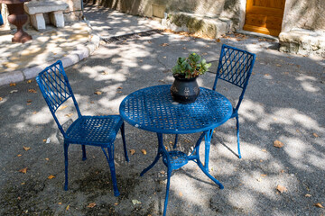 Table de bistro en métal peint en bleu avec ses deux chaises à l'ombre d'un arbre