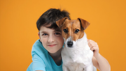 Portrait of happy smiling boy and dog Jack Russell Terrier hugs her with tenderness and look at camera on yellow background. Pets. Emotions of people. Childhood. Life style. Pet care