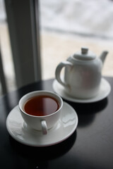 white cup with black tea and teapot on black table