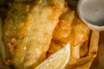 Classic crispy deep fried fish and chips with lemon and tartar sauce white dish on a wooden table