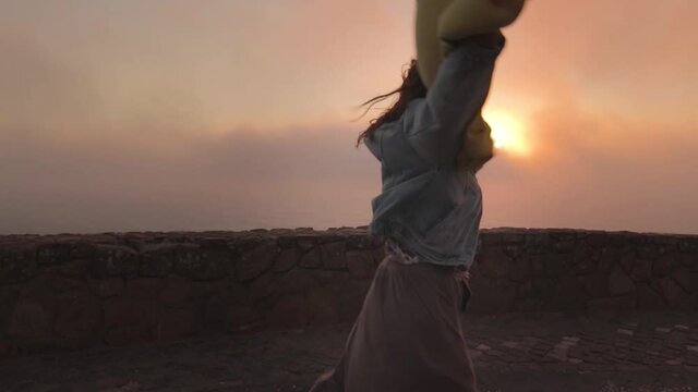 mujer bailando alegre al atardecer con mucho viento en un acantilado de Cabo da Roca, Portugal.