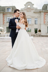 beautiful, gentle and happy bride and groom hugging on background of building