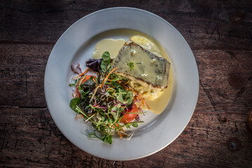 Gourmet garnished grilled salmon with salad mash potato on a white dish wooden table
