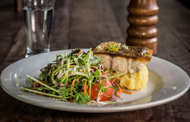 Gourmet garnished grilled salmon with salad mash potato on a white dish wooden table