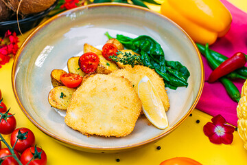 Breaded chicken fillet with spinach potatoes and tomatoes on a decorated table
