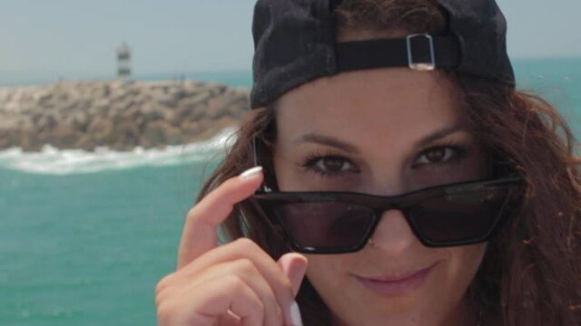 Mujer joven con gafas de sol y gorra y vaqueros en Playa de Nazar&eacute;, en Portugal