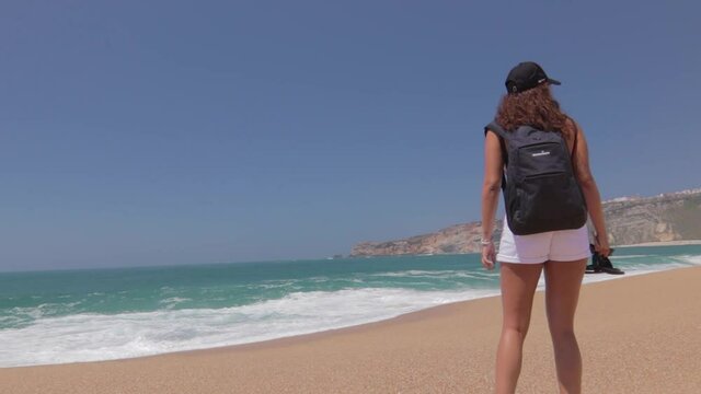 Mujer joven caminando  en ba&ntilde;ador y vaqueros en Playa de Nazar&eacute;, en Portugal