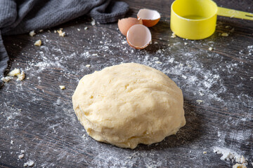 Gnocchi preparation steps: Homemade gluten free mashed potato puree dough on dark table. Flour, measure cup, towel and eggshells in the background. Creating authentic pasta dough for an Italian dish.