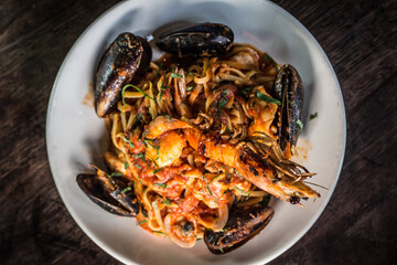 Linguine spaghetti marinara seafood dish with prawn, mussels, parsley, tomato on a white dish and wooden table