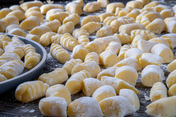 Gnocchi preparation steps: Raw uncooked handmade gluten free potato gnocchi on a dark table with sprinkled flour on top. Creating authentic pasta dough for an Italian dish. Side view.