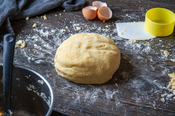 Gnocchi preparation steps: Homemade gluten free mashed potato puree dough on dark table. Flour, scraper, measure cup, eggshells in the background. Part of creating pasta dough for an Italian dish.