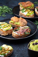 Assorted bruschetta with various toppings on a dark plates on dark background. Appetizing bruschetta. Mediterranean cuisine. Top view