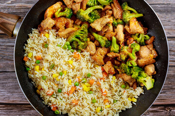 Stir-fry chicken and broccoli with rice in pan on wooden background.